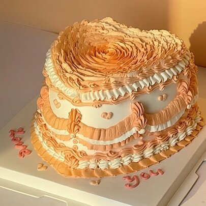 A white and peach heart shaped cake with piped details. 