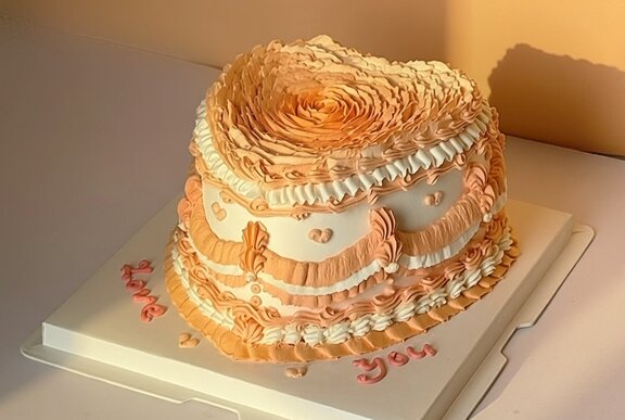 A white and peach heart shaped cake with piped details. 
