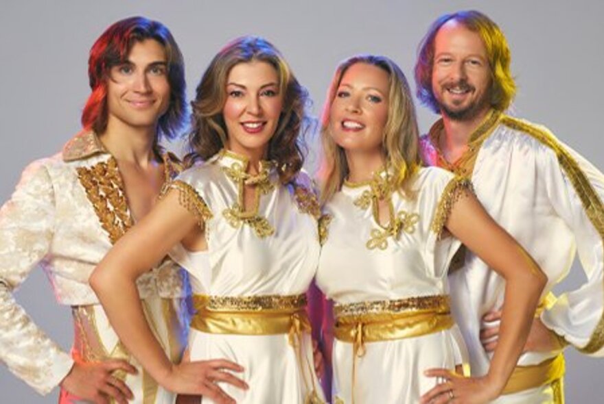 ABBA tribute band BABBA dressed in white and gold tunics with their hands on their hips.