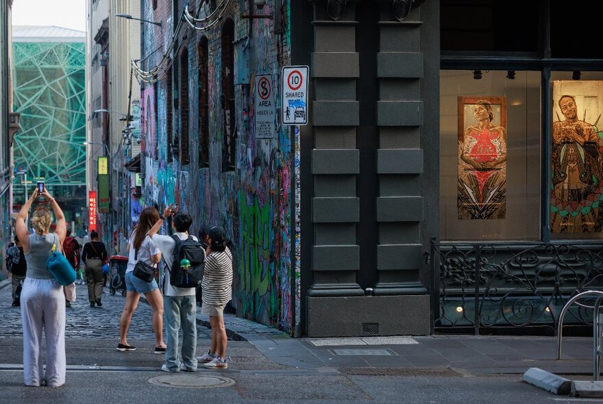 People standing at the corner of Hosier Lane and Flinders Lane with a view of a lit-up street art exhibition.