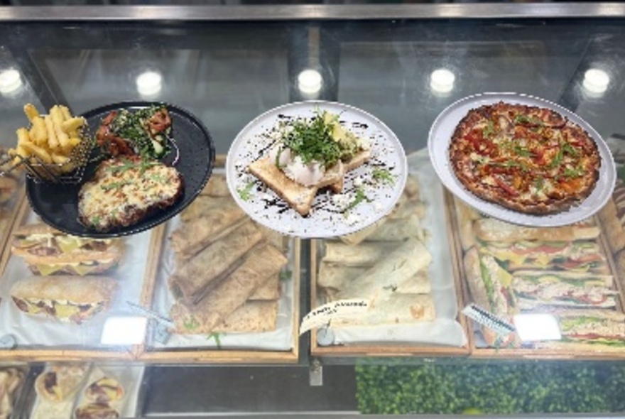 Three plates of food lined up on a glass counter including pizza, chips, and  a cooked egg breakfast.