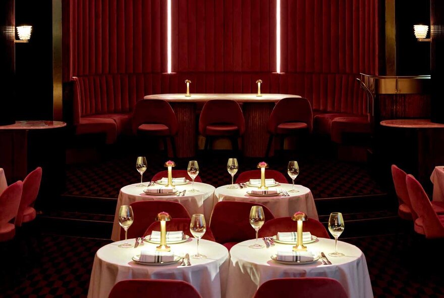 A small, red cabaret lounge with round tables set with glasses. 