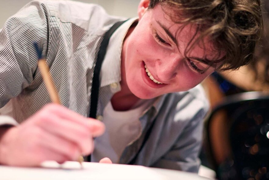 Close-up of a teenager concentrating on drawing with a pencil on paper.