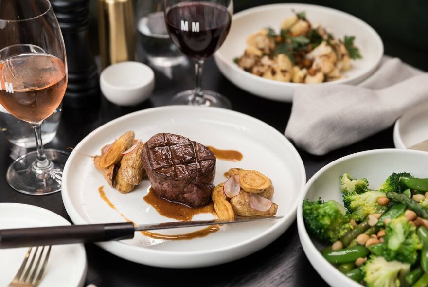 Steak, vegetable and pasta dishes on a table with wine