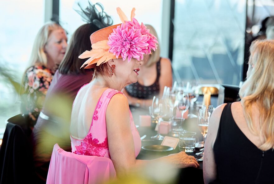 Women dressed in race day fashion and fascinators celebrating at a table at Eureka 89, seated against floor to ceiling windows. 