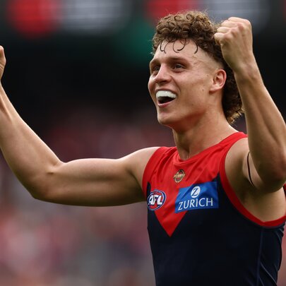 A Melbourne AFL football player on the field during a match with his arms in the air cheering himself on.