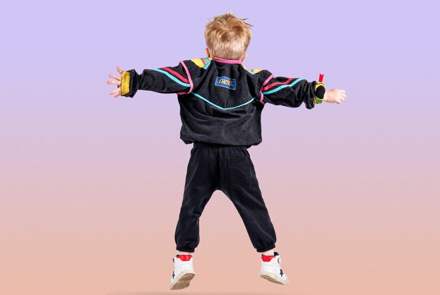 The back of a young boy mid jump, with his arms outstretched. 