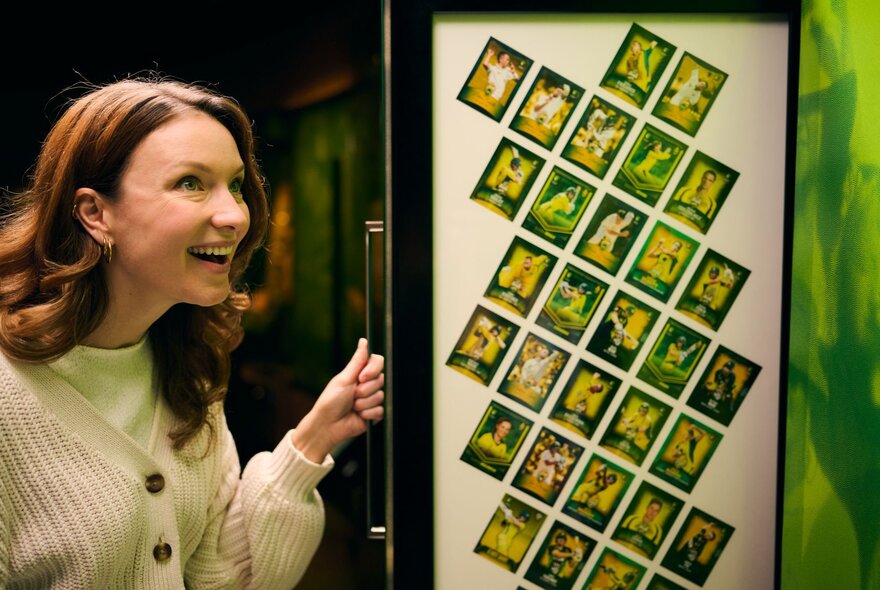 A smiling woman opening a door with collectible cards of cricket players on the back of it.