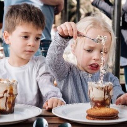 Two children seated at a table, enjoying decadent iced chocolates and large cookies with chocolate cream filling.