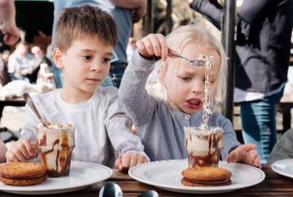 Two children seated at a table, enjoying decadent iced chocolates and large cookies with chocolate cream filling.