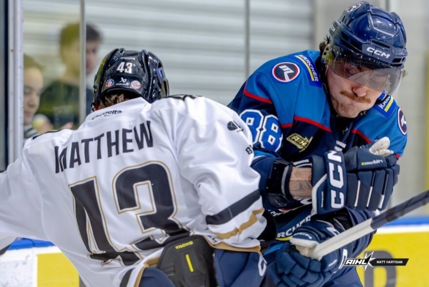 Two ice hockey players from opposing teams battling it out on the ice.