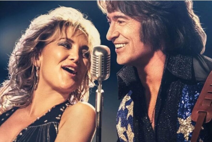 Hugh Jackman and Kate Hudson performing as Neil Diamond and singer with microphone.