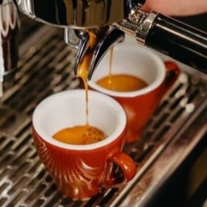 Two espresso coffees being poured from a barista-style coffee machine into small red mugs with white interior.