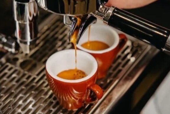 Two espresso coffees being poured from a barista-style coffee machine into small red mugs with white interior.