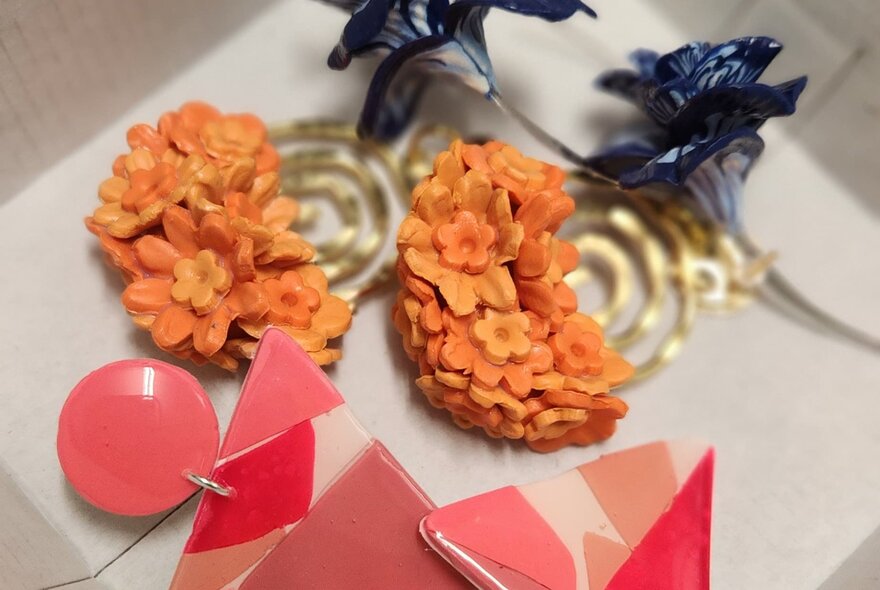 Polymer clay earrings with tiny orange flowers and another pair with geometric shapes in red and pink.