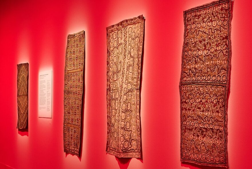 A gallery space with red walls and woven fabric pieces hanging on the walls. 