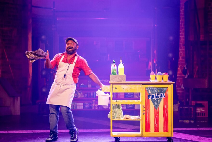 A performer singing while pushing a food cart prop, on a theatre stage.