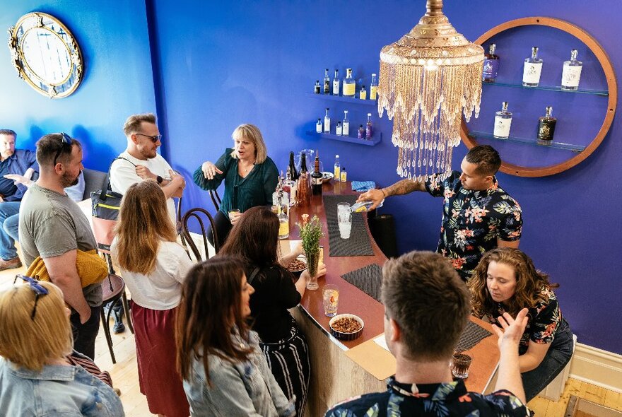 Patrons at a gin bar with blue walls, chandelier and curved bar.