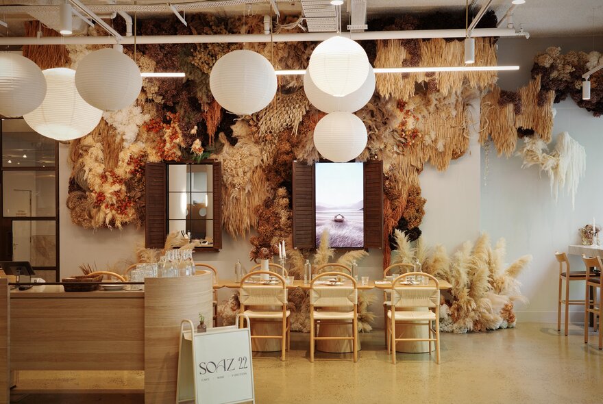 Light-filled interior of Soaz 22 cafe, with pale blonde wood tables and chairs, round hanging lighst and straw-coloured foliage hanging from the celling.