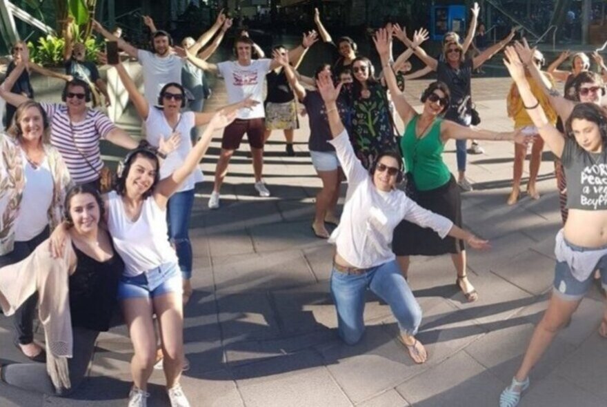Silent disco tour participants wearing headphones and posing with arms and legs outstretched in a public space.