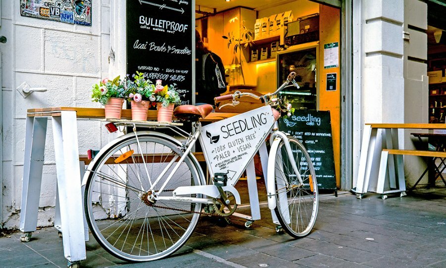 A cafe with a bicycle outside holding plants and a sign.