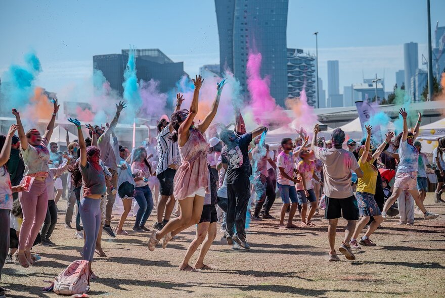 Crowds jumping up in the air while throwing colourful powders at a city Holi festival.