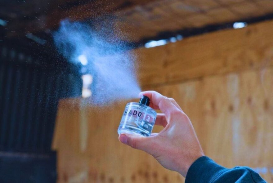 A hand spraying perfume from a small bottle into the air, at a perfume making workshop.