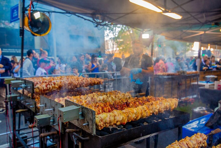 Someone cooking meat on long barbecues at a festival.