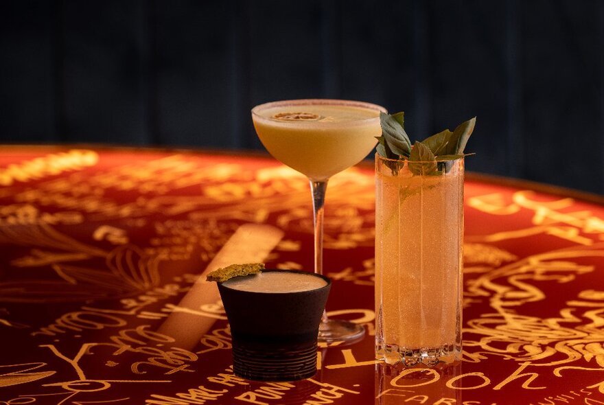 A table with etched patterns and letters holding three different cocktails. 