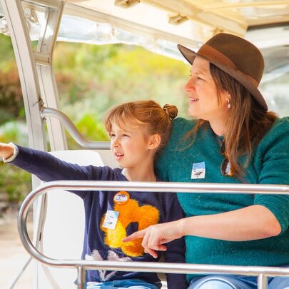 An adult and child riding in an open bus, the child pointing at something. 
