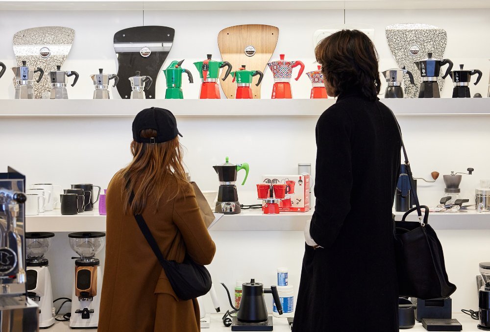 Two people looking at a display of colourful coffee pots.