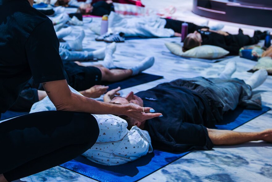 People laying on their backs on yoga mats on the floor, in a guided breathwork meditation session.