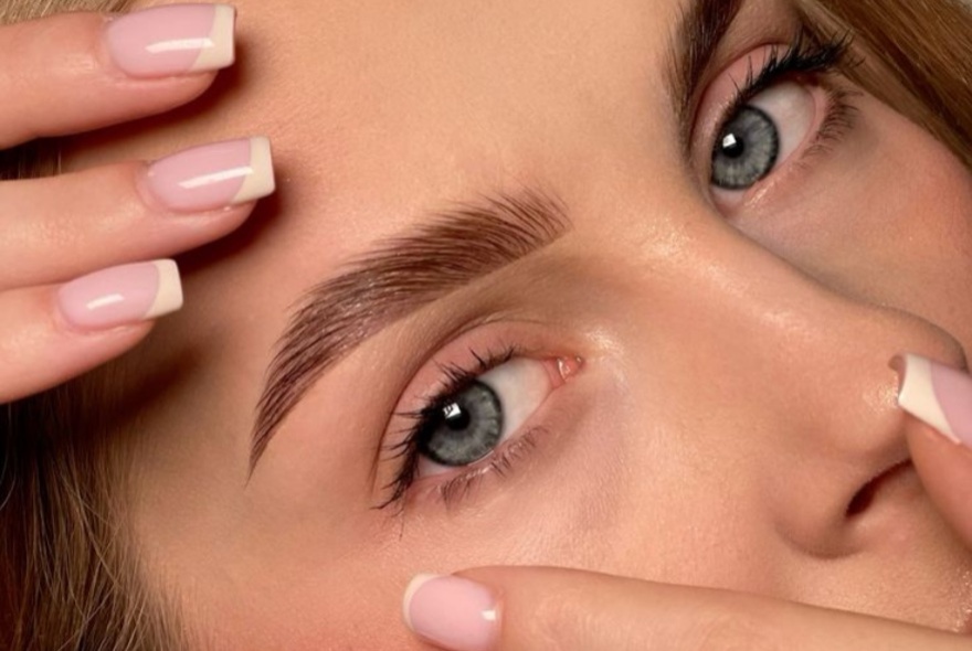 Manicured hands holding a woman's face in a tight shot that features her eyes and perfect brows.