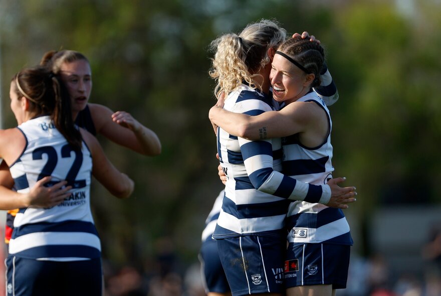 Geelong AFLW players celebrating on the football field after a goal by hugging each other.