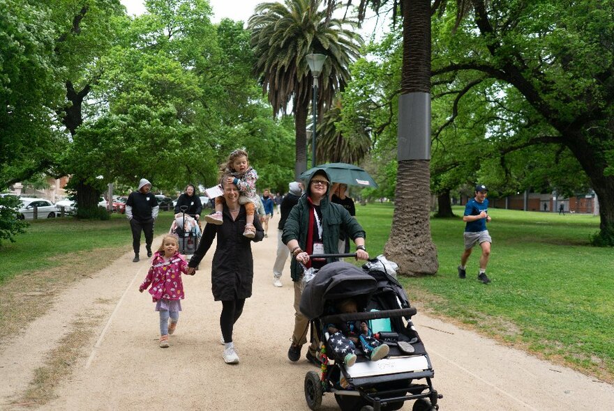 People walking in a charity walk in a park with gravel path, trees and grass.