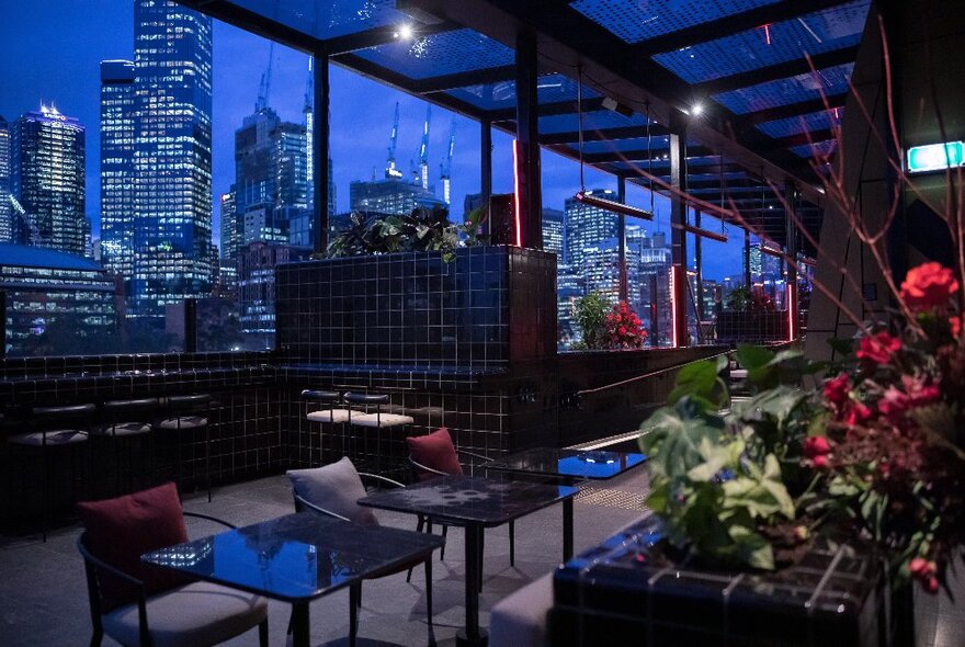 An empty rooftop bar at night with a view to city buildings.