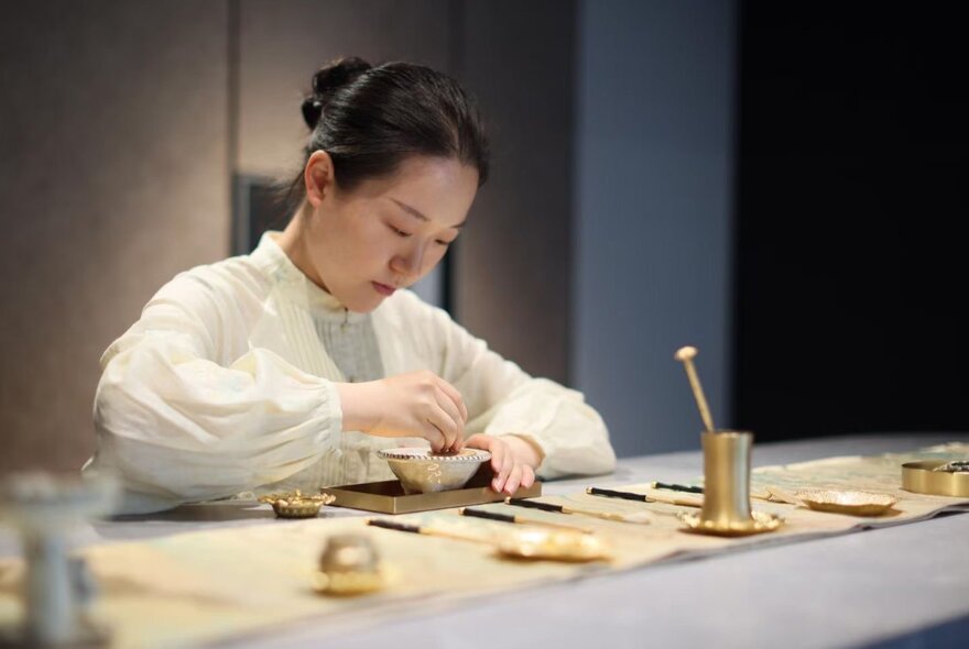 Chinese perfumier working with metal bowls and instruments on a bench.