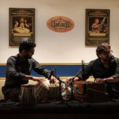 Two seated musicians performing North Indian classical music on a tabla and harmonium inside a restaurant.