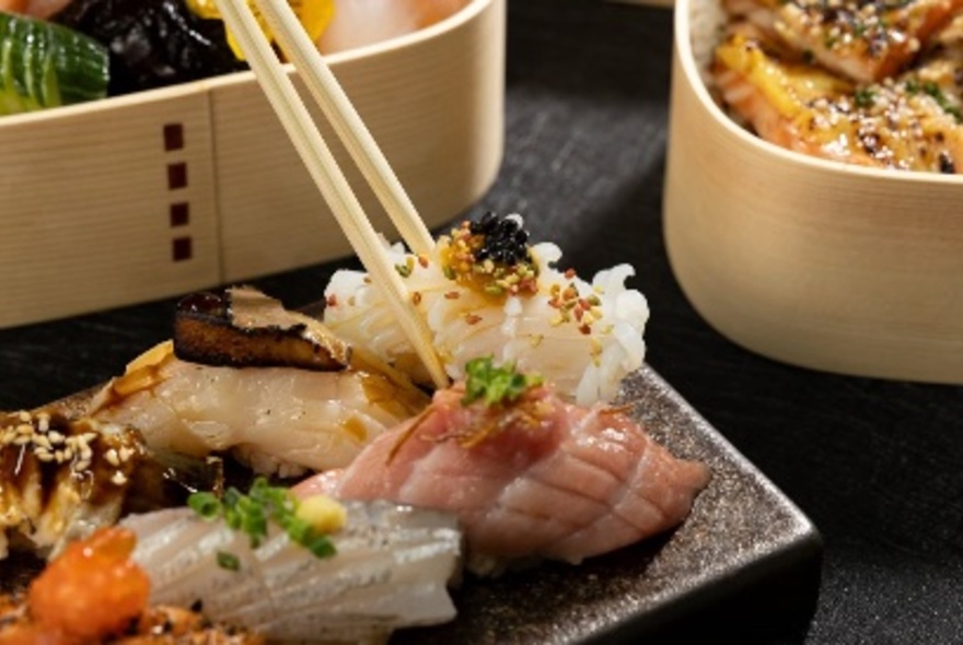 Chopsticks picking up sashimi from a plate of assorted fish, with steamers in the background.