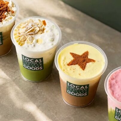 A row of coffee and matcha drinks in branded takeaway cups.