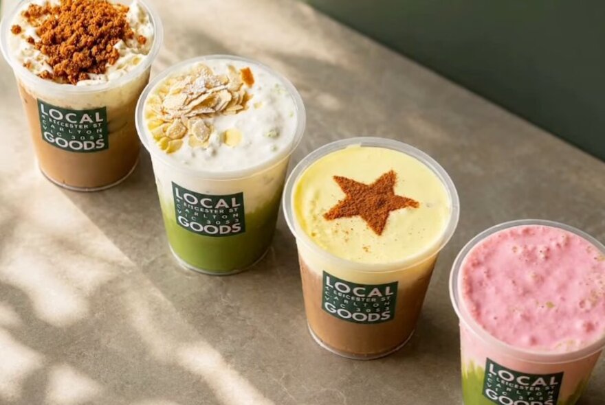 A row of coffee and matcha drinks in branded takeaway cups.