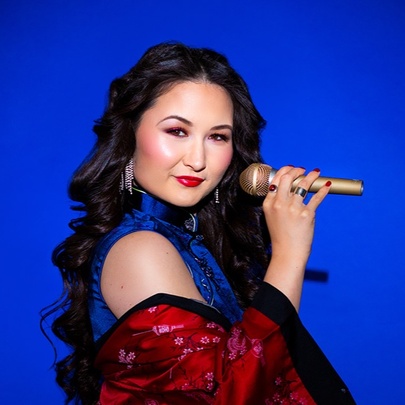 Comedian and cabaret artist Kelly Lim Harris holding a microphone against a vivid blue background. 