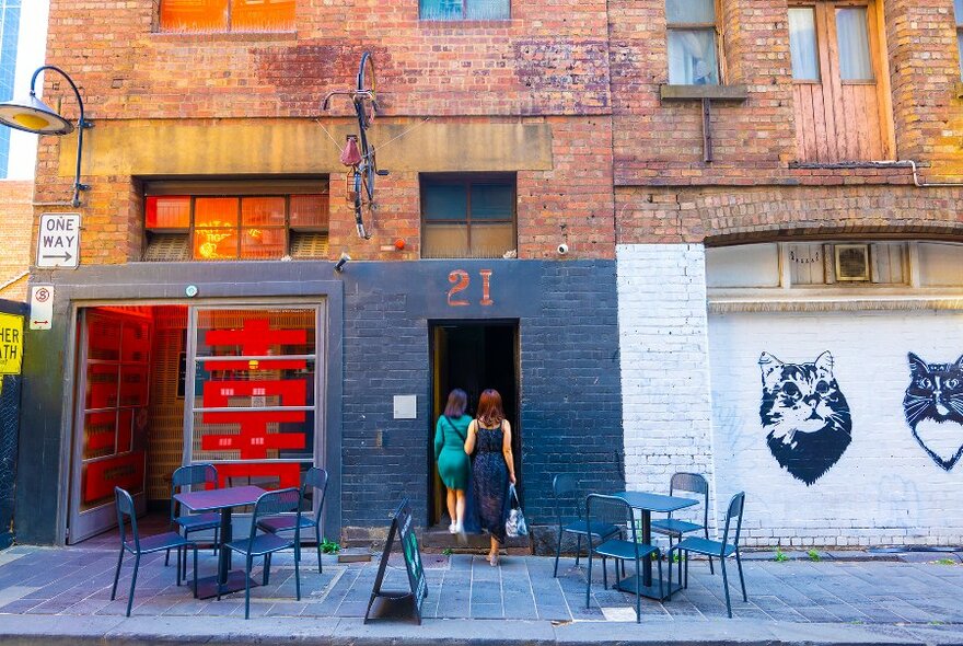 Two women walking into a bar in a laneway.