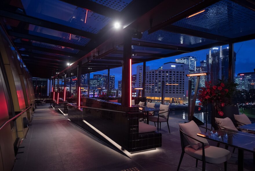 The outdoor terrace at Ocean's 12 with couch seating, table and chairs and background views of city buildings in dusky twilight.