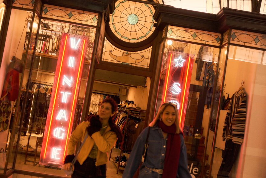 Two women exiting a vintage shop with neon signs.