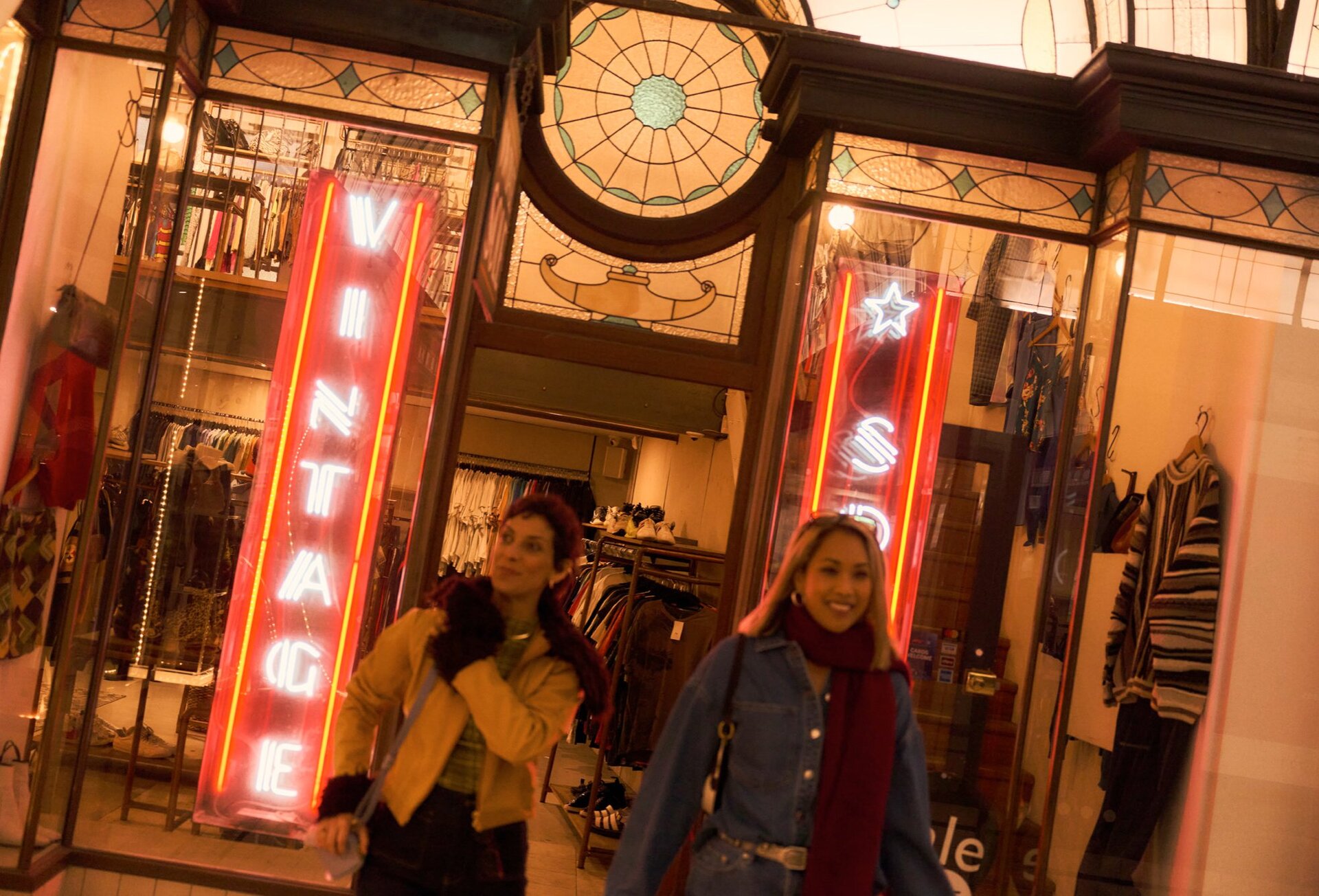 Two women exiting a vintage shop with neon signs.