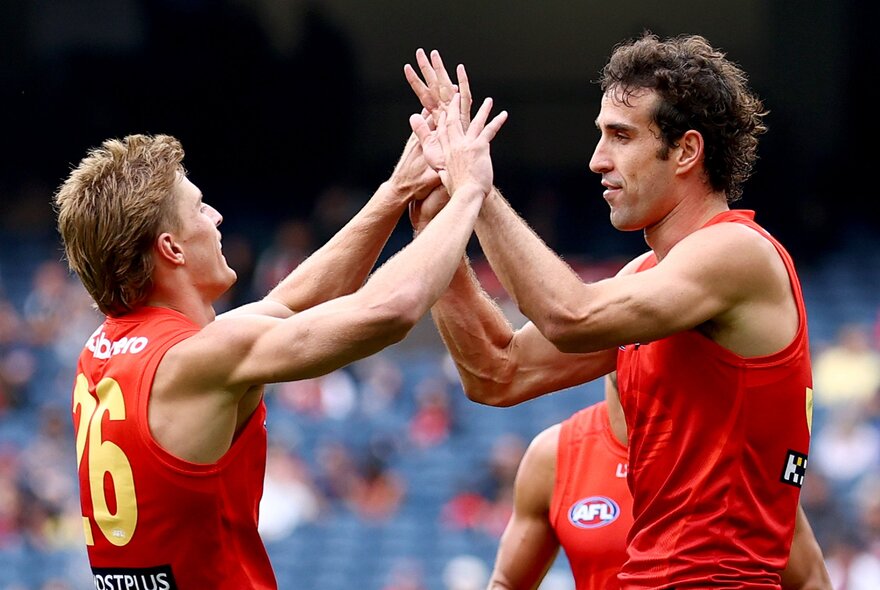Two Gold Coast Suns players slap hands in congratulation during a match. 