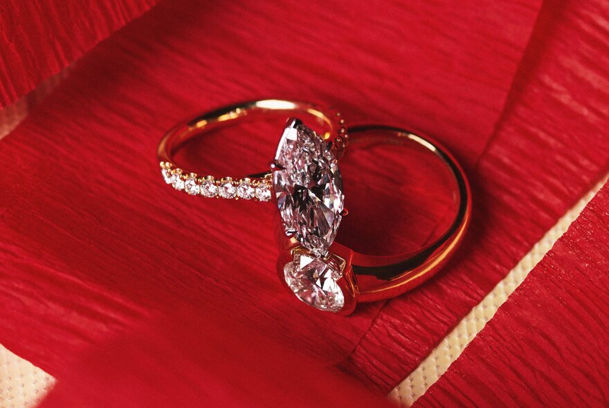 Two engagement rings resting together on red fabric.