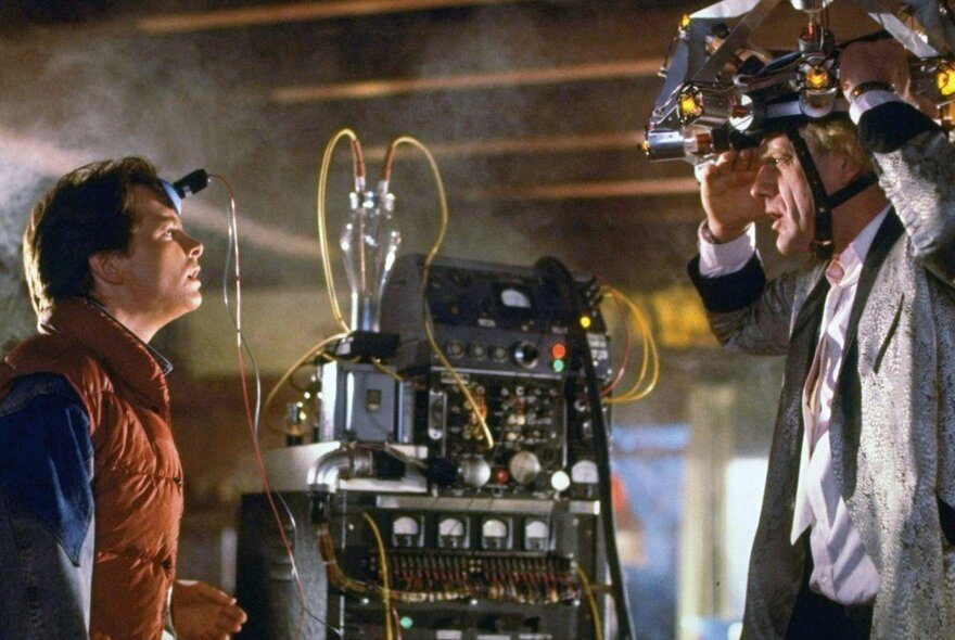 A scene from the movie 'Back to the Future'' with the two main actors facing each other in profile with a time machine computer standing between them.