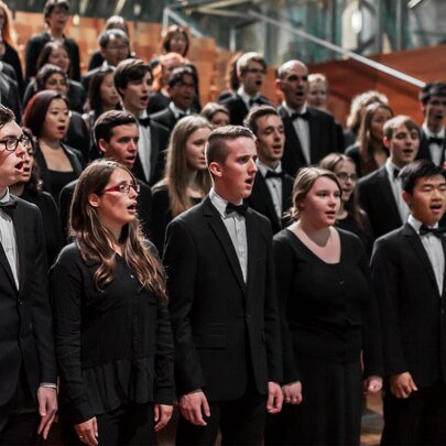 Large choir standing in rows singing, wearing formal black suits and dresses.